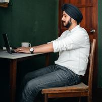 A man with a  turban typing on a laptop on a wooden table