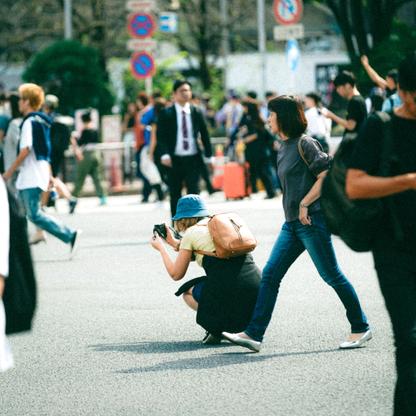 A woman taking a picture crouched down on a busy street