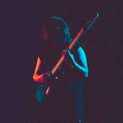 A man with long dark hair plaiyng electric guitar on a dark stage