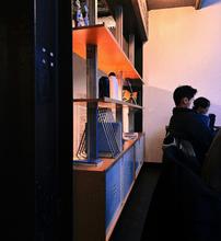 Two men work on a computer in the back of a dim room next to a shelf