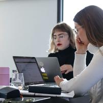 Two women work on laptops at the corner of a table