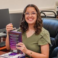 An author smiling while holding books at a computer desk