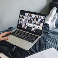 A Zoom call with many participants shown on a grid on a laptop in someone's lap