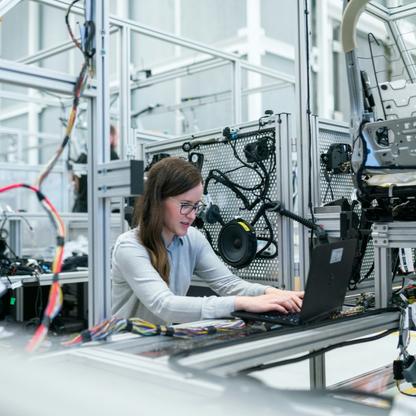 A woman typing on a laptop surrounded by various machinery