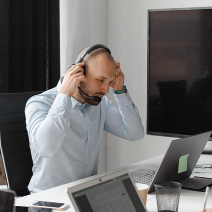 A bald man sitting at a table with a laptop putting on a headset