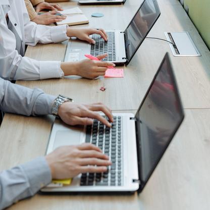 Three people typing/writing at a long table