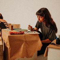 A woman carefully painting small objects at a table