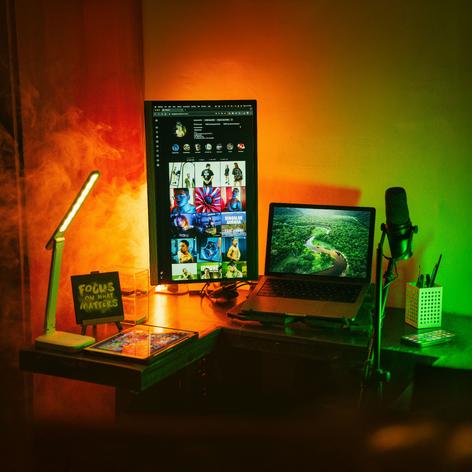 A computer with a vertical monitor and microphone to either side on a colorfully lit corner desk