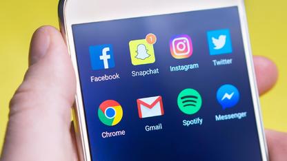 Hand holding a cell phone with social media icons on the screen