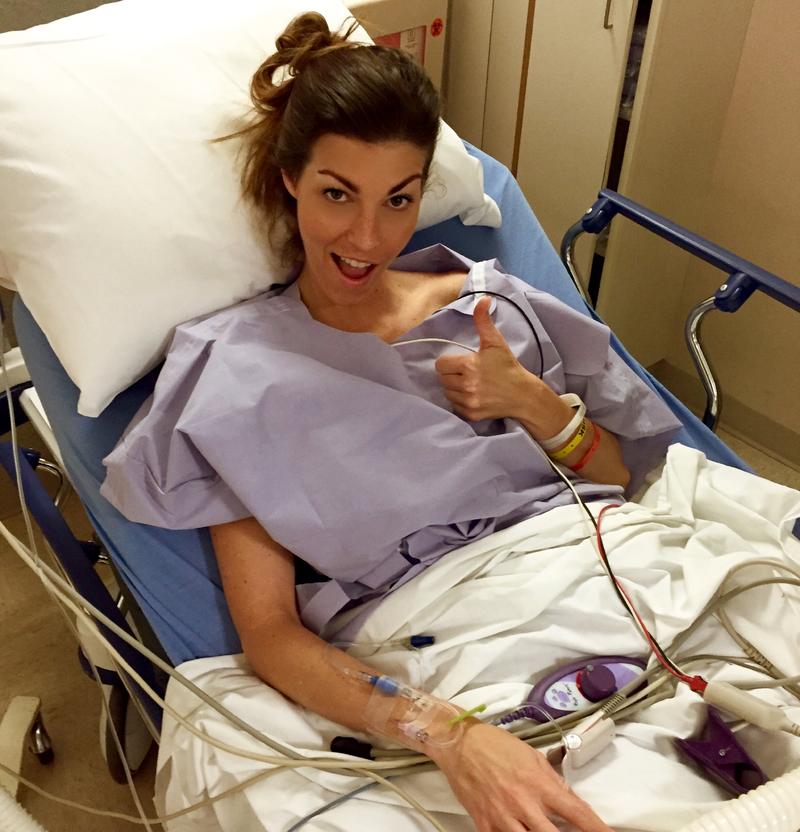 Heather in a hospital bed giving a thumbs up