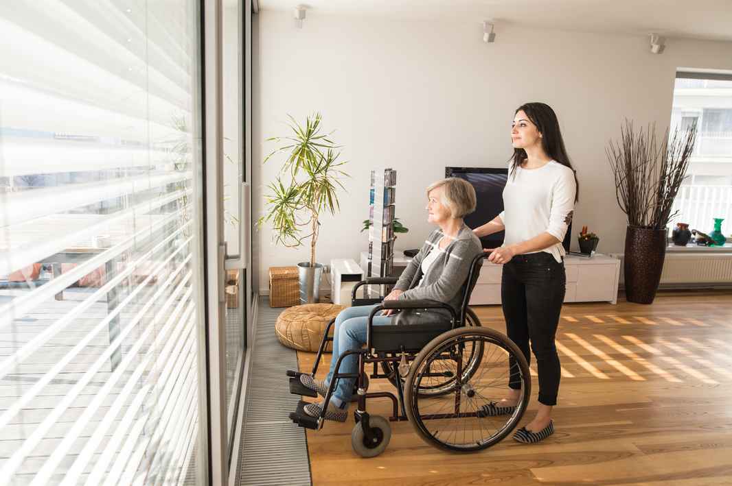 graphicstock-disabled-senior-woman-in-wheelchair-at-home-in-her-living-room-with-her-young-daughter-caring-for-her-looking-out-the-window_BuMnN_8MZ
