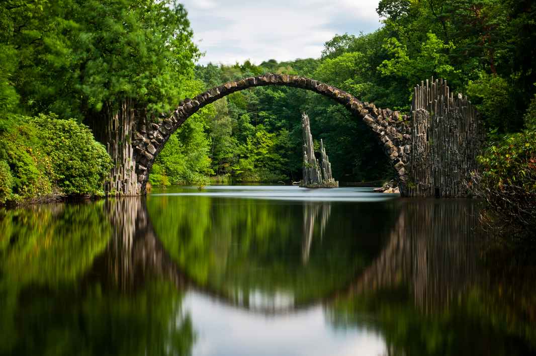 very-old-stone-bridge-over-the-quiet-lake-with-its-reflection-in-the-water-37944293