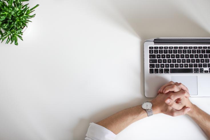 Desk with laptop and woman's clasped hands