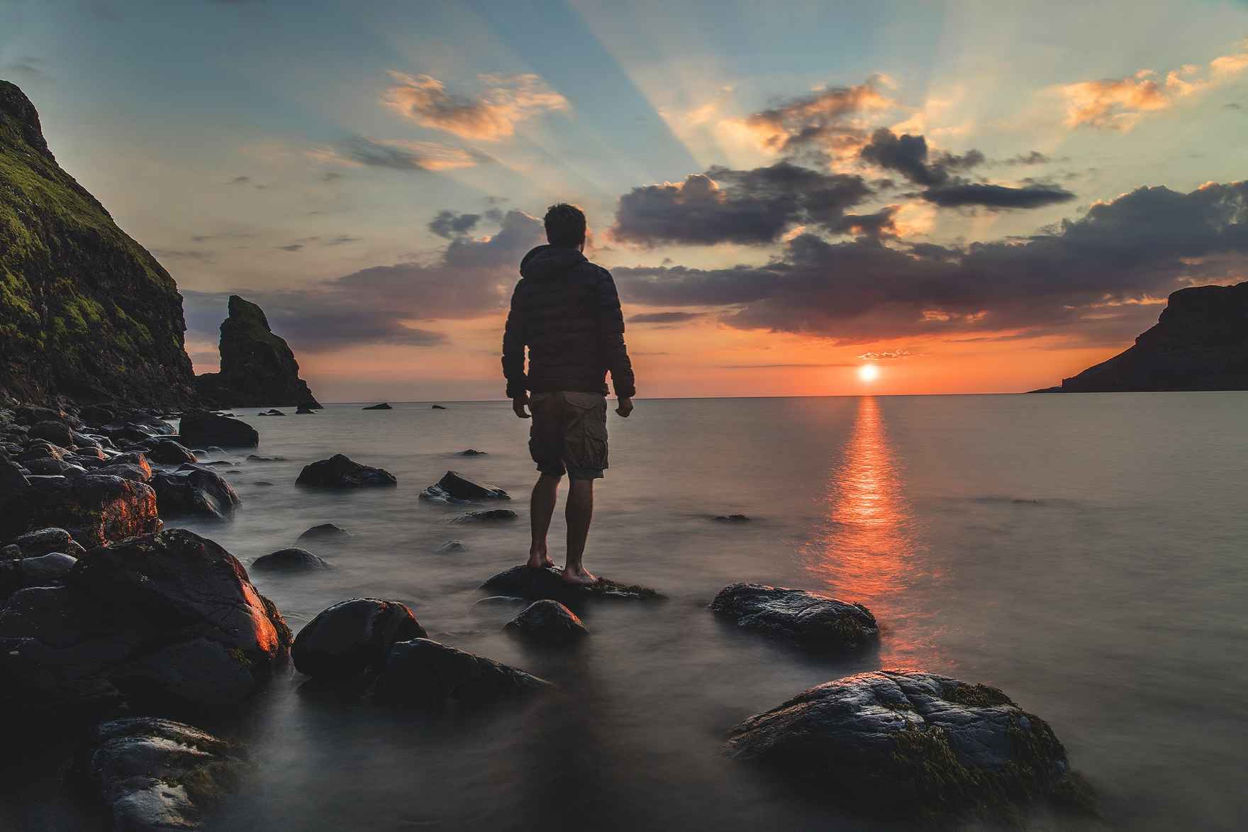 Man standing at edge of water looking at sunset