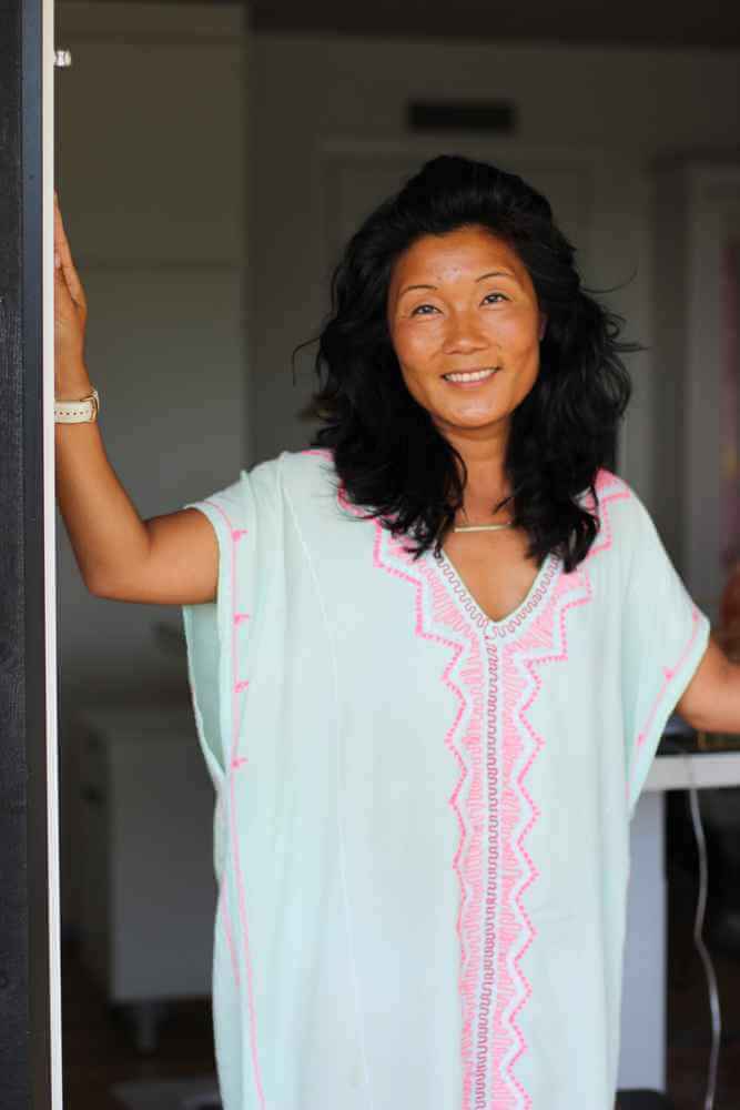 Asiatisk kvinde med mintgrøn og pink kjole på står i en døren og smiler
