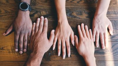 Five different hands with a variety of skin tones resting face down next to each other on a table