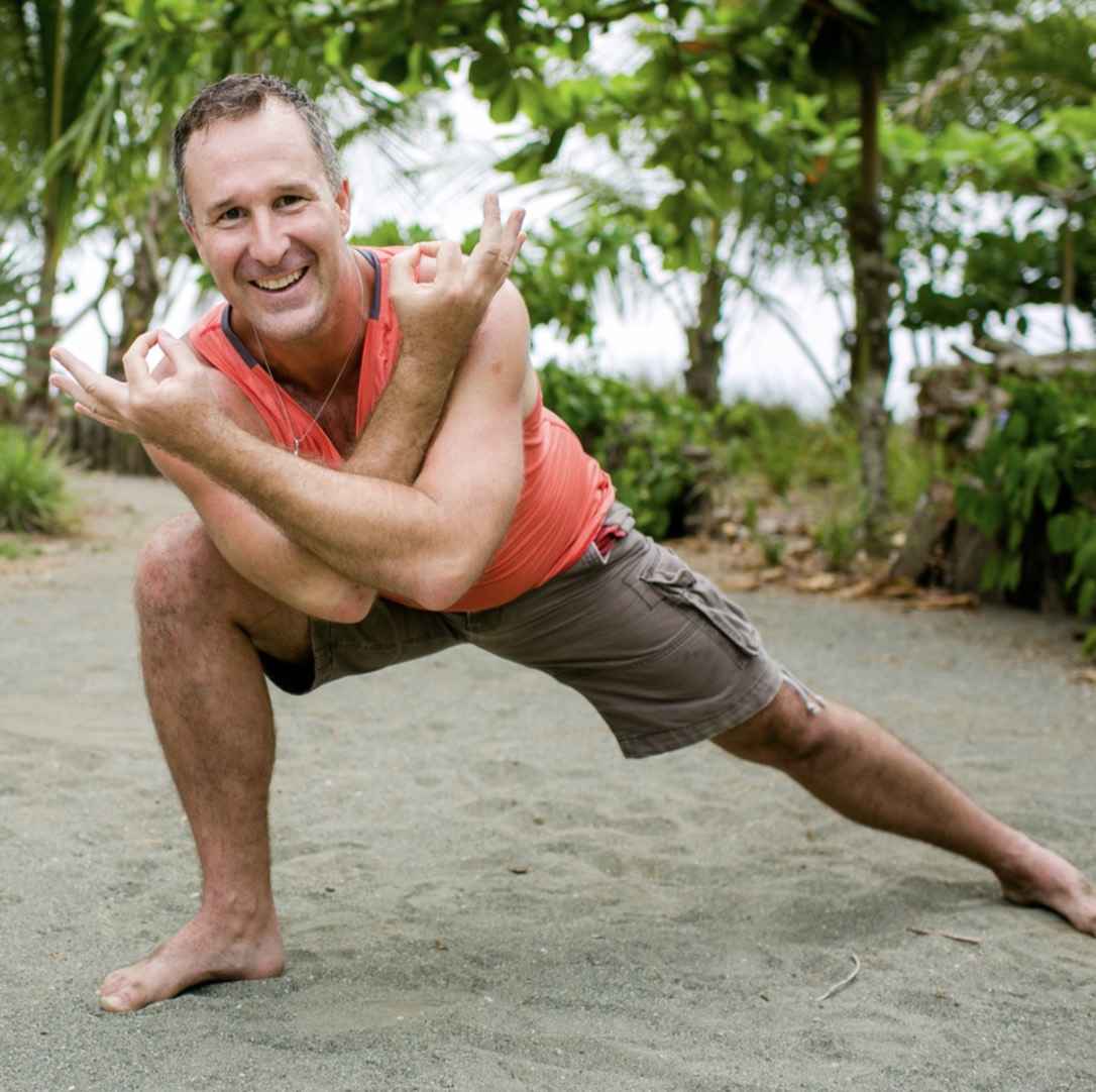 Yogi Aaron doing a warrior pose with an orange shirt on smiling