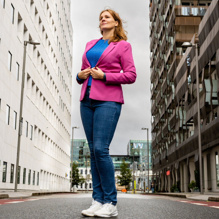 Bilde av Paro som står med rosa blazer, blå dongeri og hvite joggesko. Hun står midt i gata og ser opp på skrå mot himmelen.