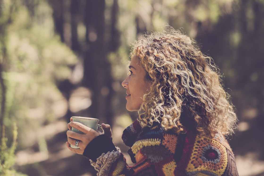 Simona Pilolla sidder i skoven med en kop i hånden og kigger op og smiler