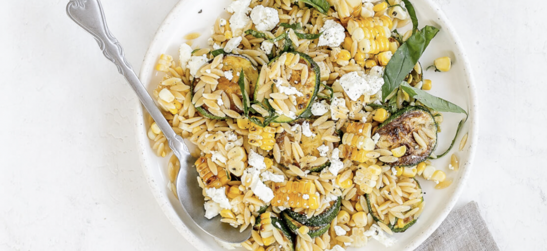 Orzo zucchini and corn salad fresh topped with goat cheese and basil in a bowl with spoon