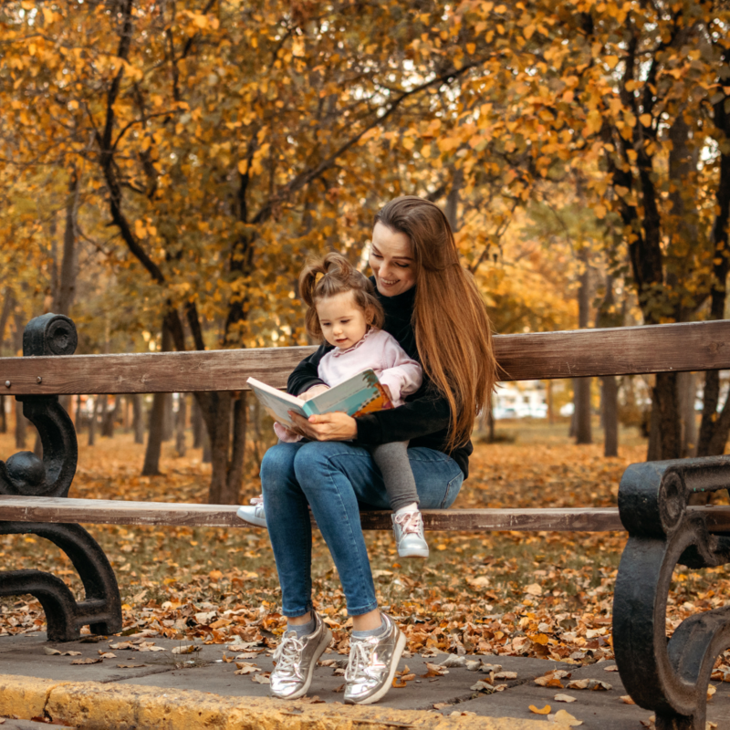 Mom and son reading on a park bench in autumn