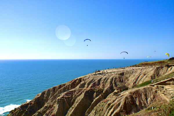 hills overlooking bright blue sea with parachute gliders