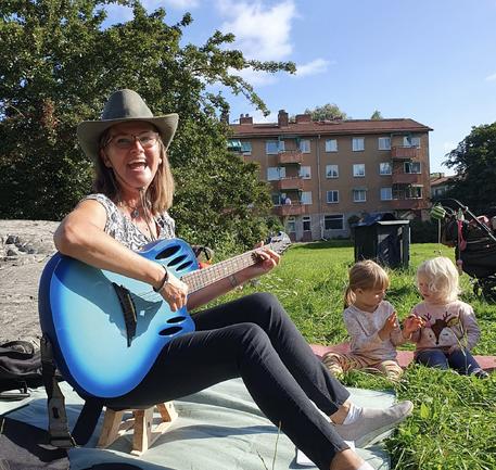 Charlotte spelar på gitarren utomhus. Några barn i bakgrunden