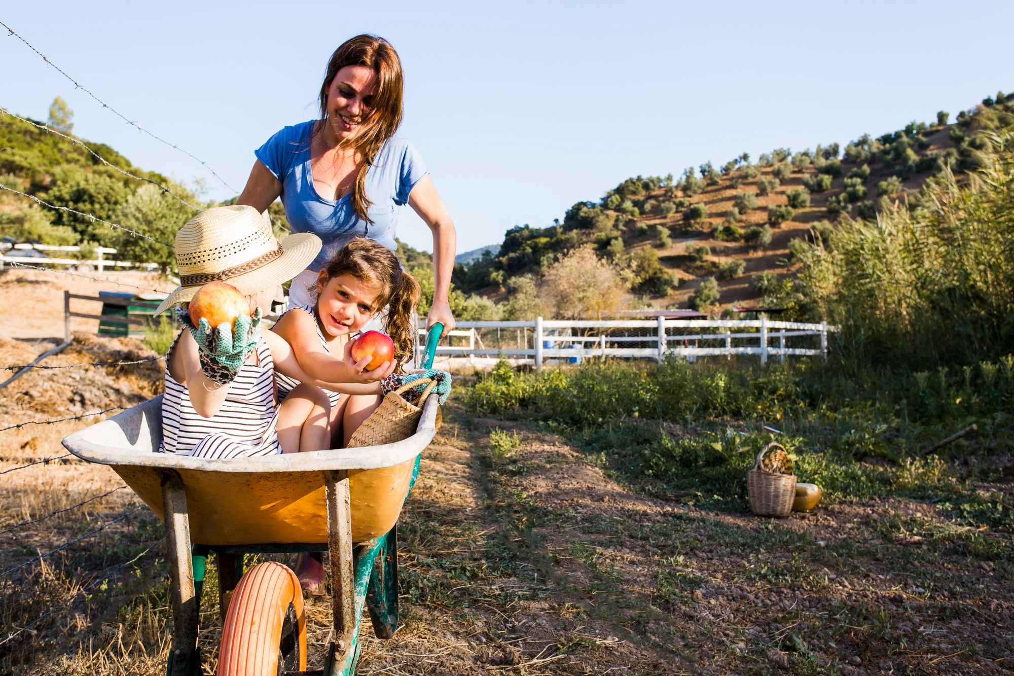 mother-pushing-her-daughters-wheelbarrow-field